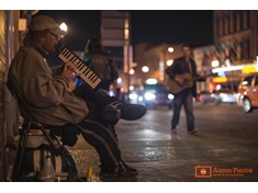 Street performer rocking out on his melodica as another artist walks by playing his acoustic guitar.